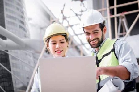 Stockbild von einer Frau und einem Mann in Arbeitskleidung und auch Schutzkleidung die sich auf einer Baustelle befinden